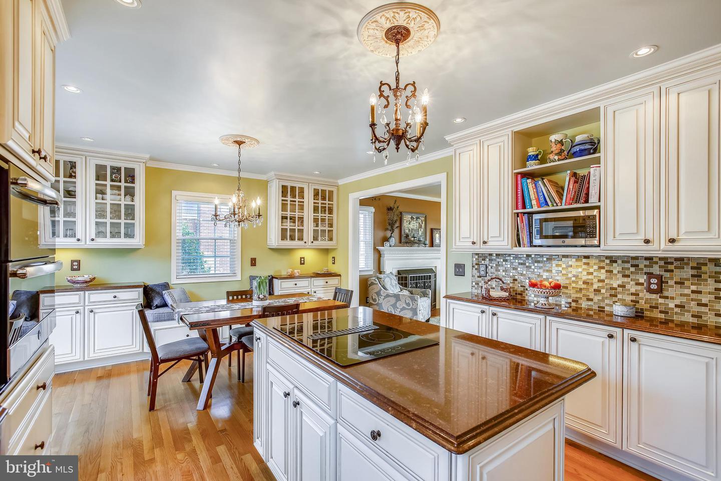 Kitchen with a large stone island, white cabinetry, colorful tile backsplash, and dining area by the window.