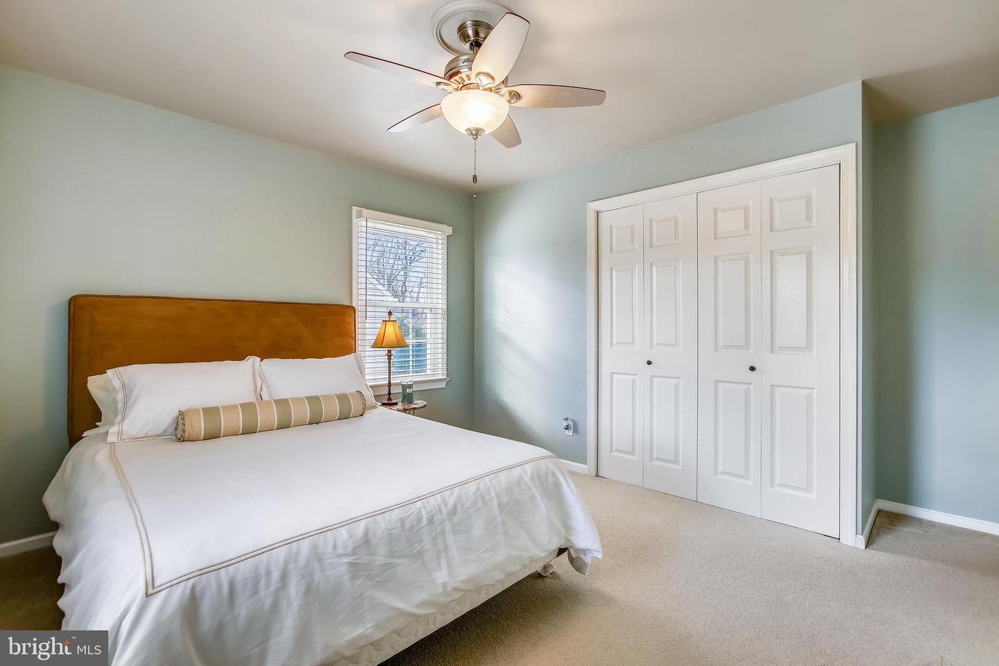 Bedroom with a white bed, ochre headboard, pale blue walls, and white double closet doors.