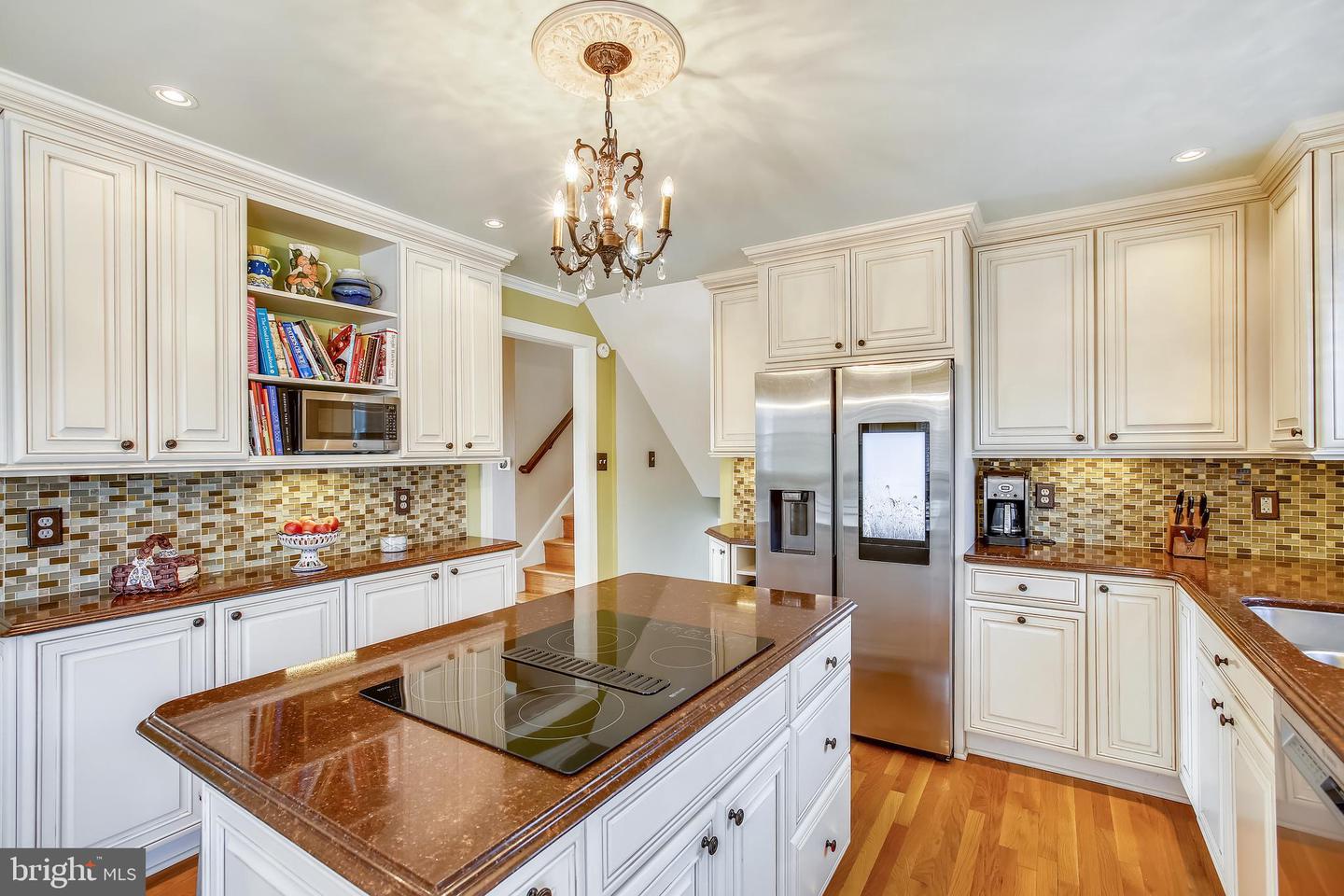 Kitchen with white cabinetry, granite counters, island cooktop, mosaic backsplash, and stainless steel refrigerator.