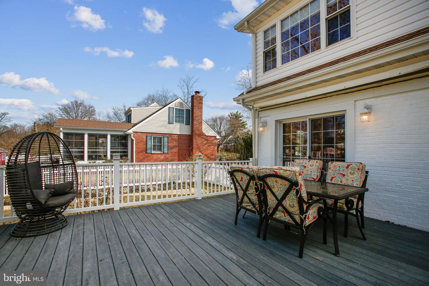 Furnished gray deck with a white railing, hanging egg chair, and outdoor dining set beside the house.