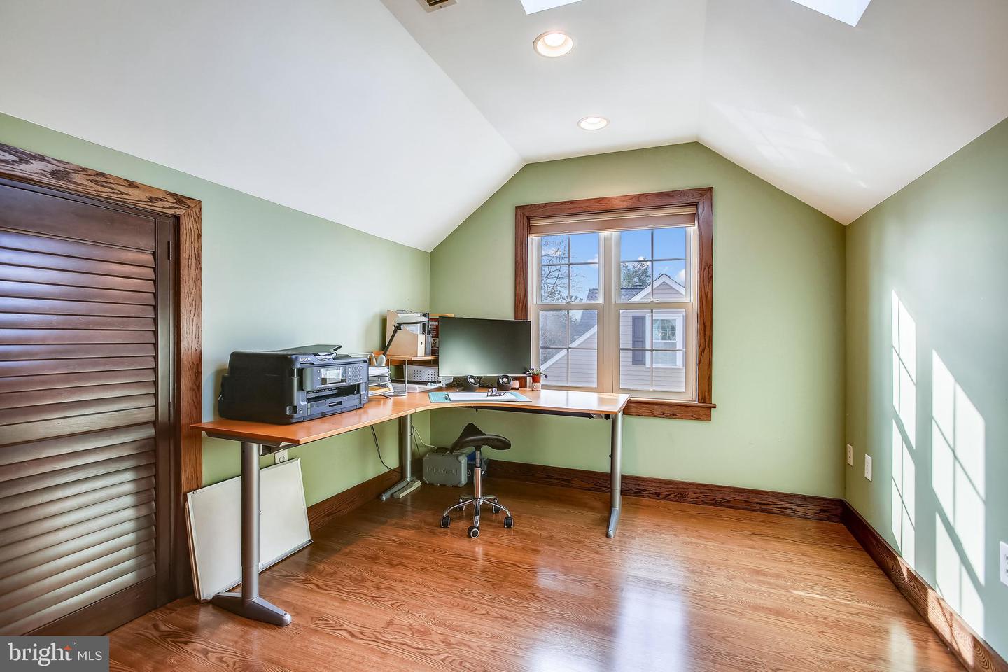 Upstairs home office with an L-shaped desk beneath a window and a vaulted ceiling.