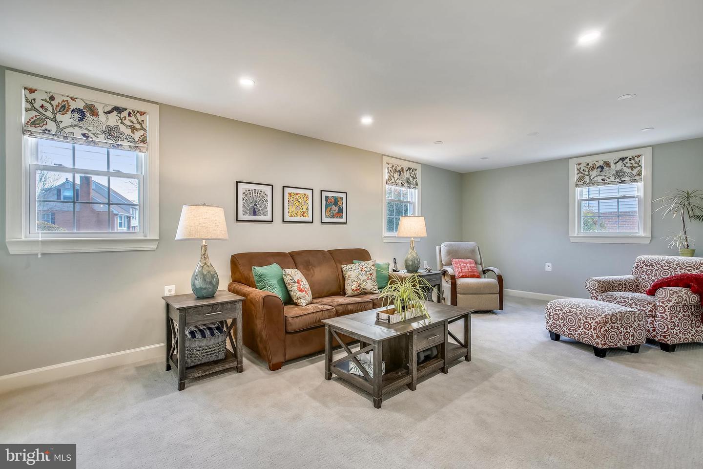Living room with a brown leather sofa, patterned armchairs, and floral window shades.