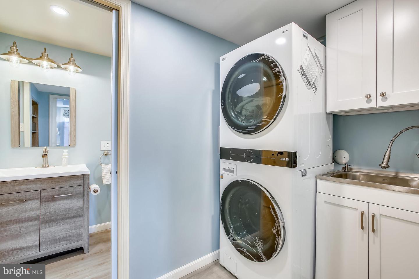 Laundry room with a stacked washer and dryer, stainless utility sink, and white cabinets.