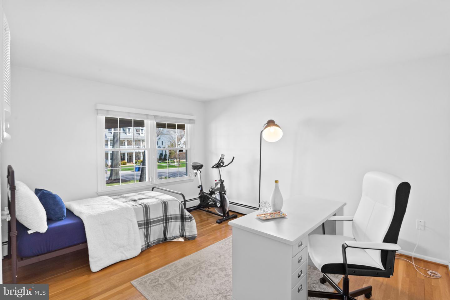 Bedroom with a desk, exercise bike, single bed, and large window.
