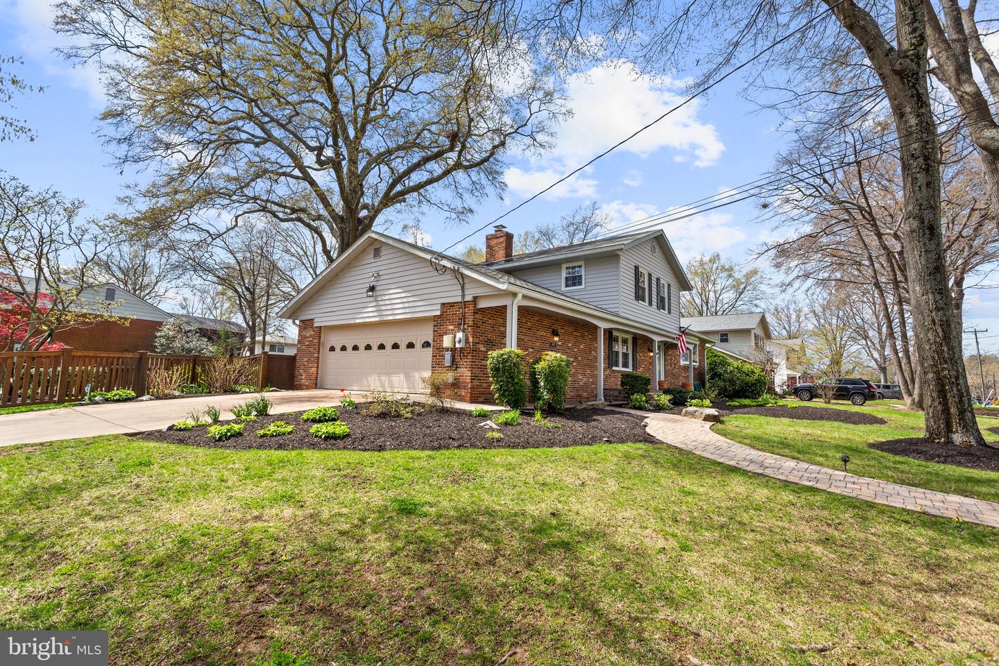 Two-story brick home with an attached garage, mature trees, and a curved front walkway.