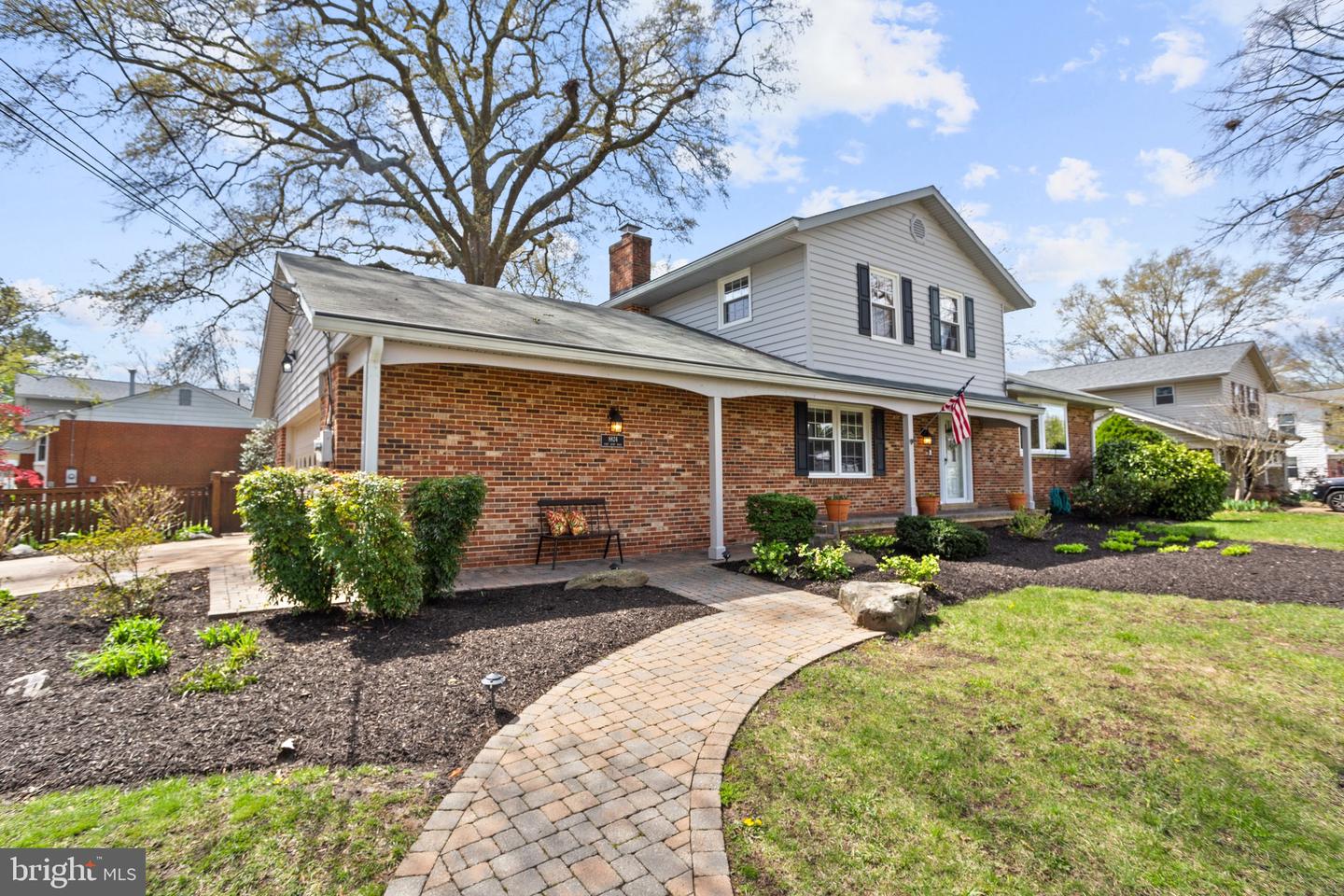Two-story brick-and-siding home with a covered porch and curved paver walkway.