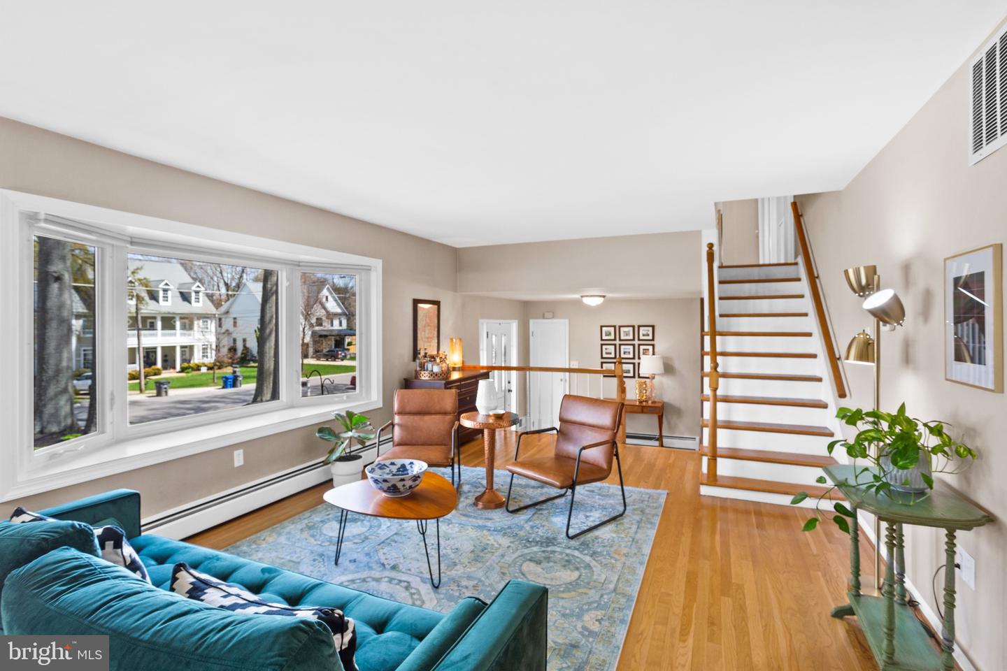 Living room with a teal sofa, leather chairs, hardwood floors, and a staircase beside large windows.