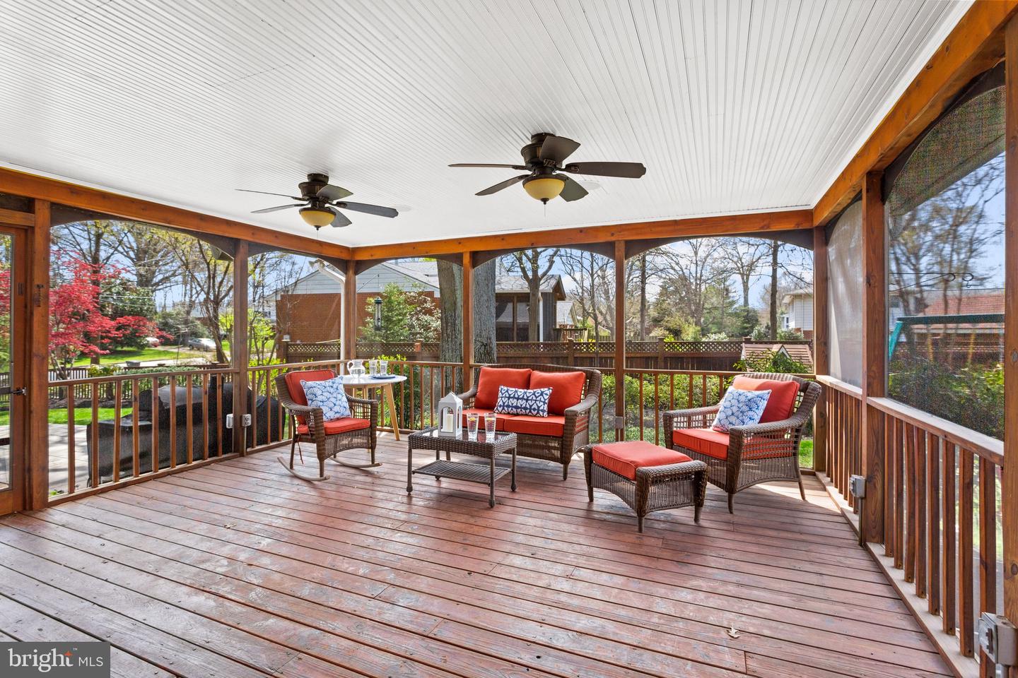 Screened porch with wicker seating, red cushions, and two ceiling fans overlooking a yard.