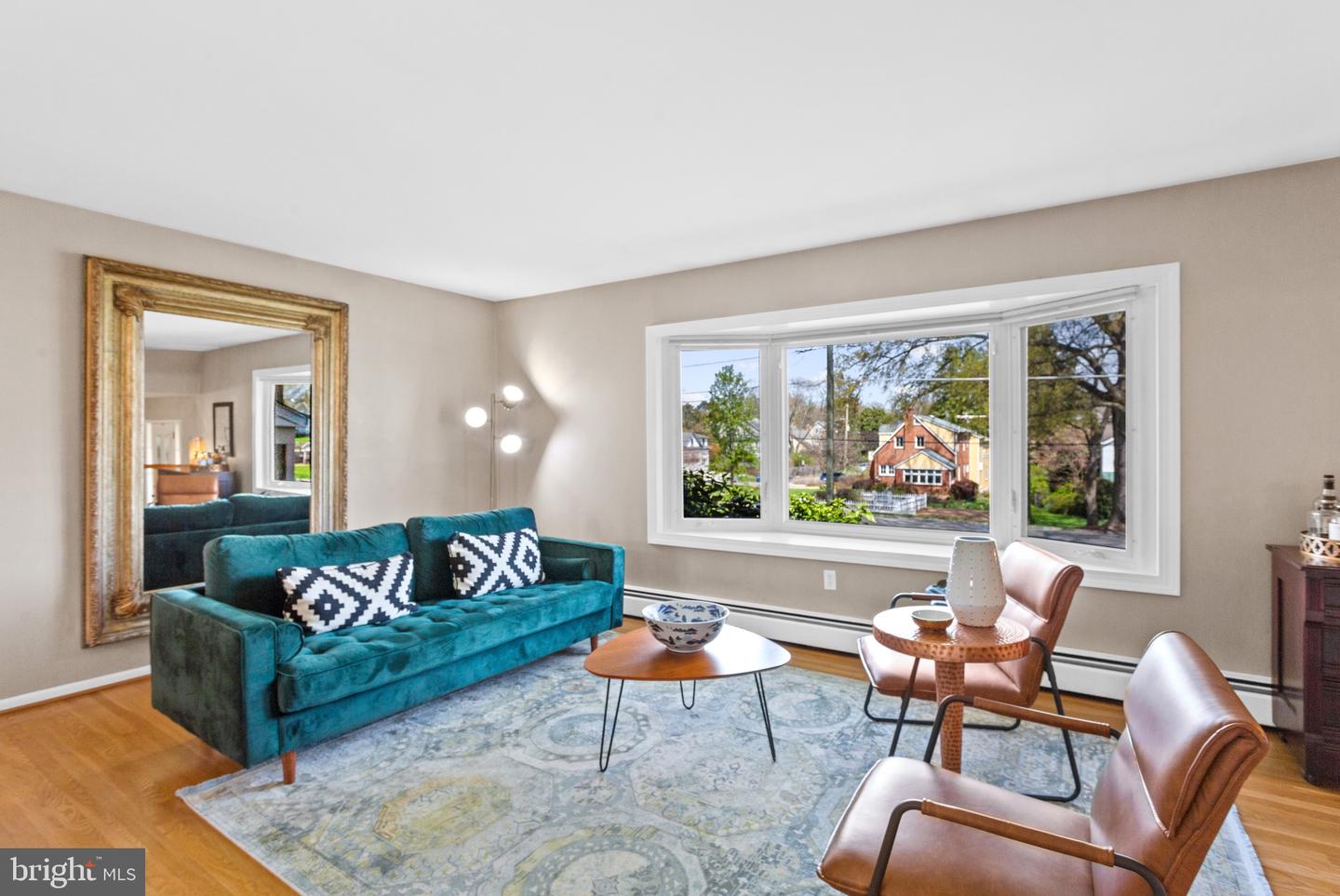 Staged living room with a teal sofa, ornate gold-framed mirror, and large picture window.