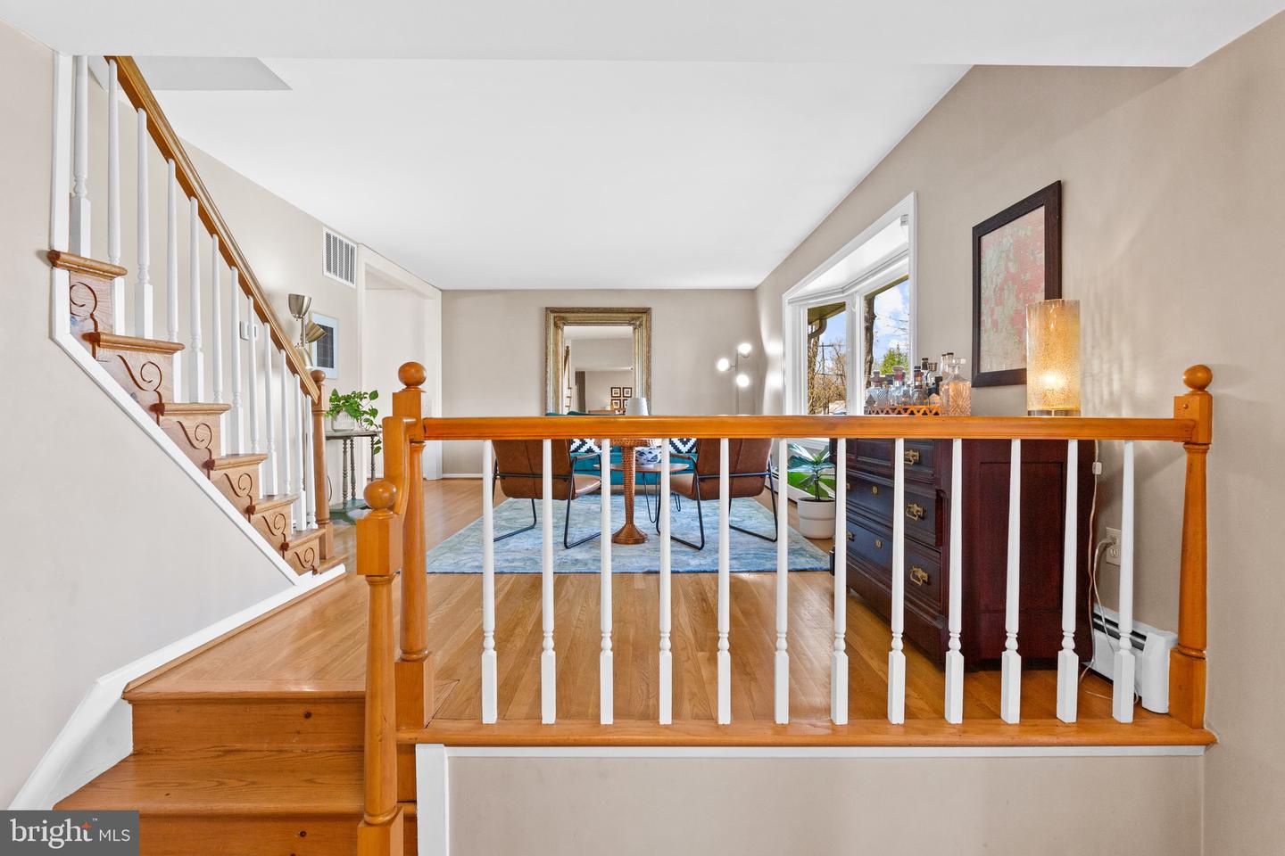 Furnished dining area with hardwood floors, a staircase, and a dark sideboard by the window.