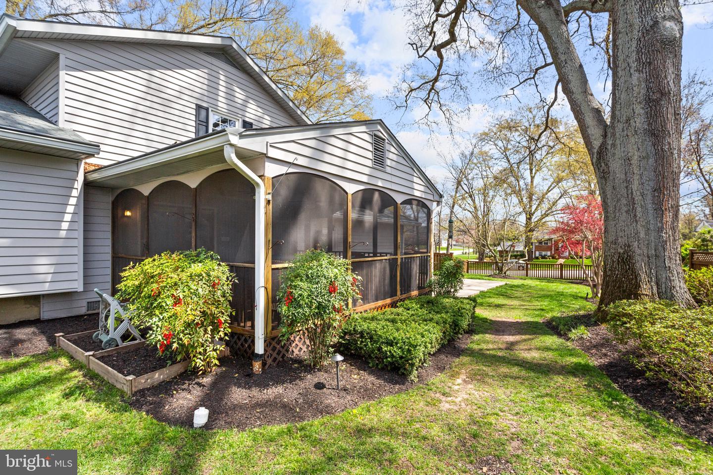 Gray-sided house with a screened porch, garden beds, and a large mature tree.