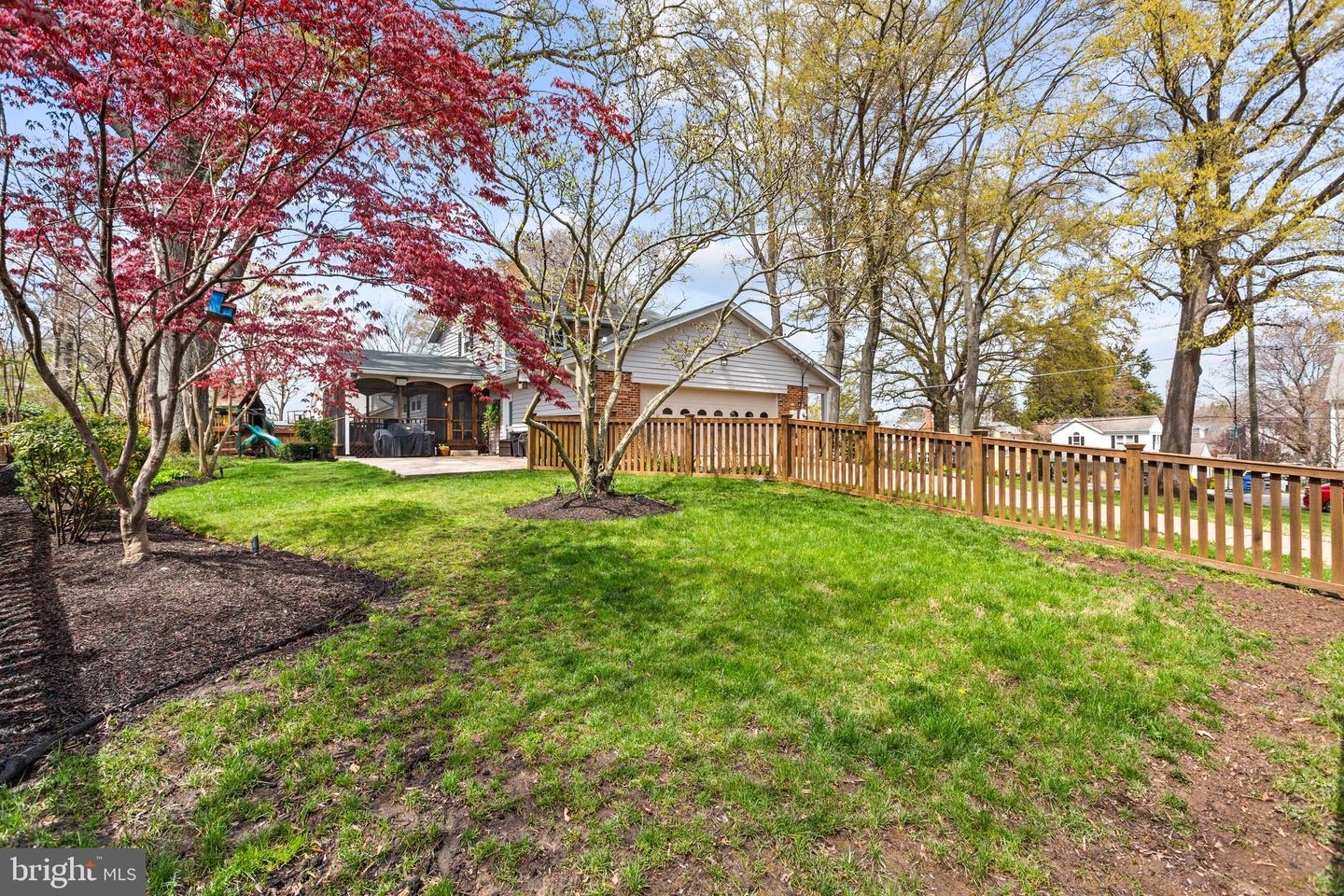 Rear of a house beyond a broad lawn, with mature trees and a wooden fence.