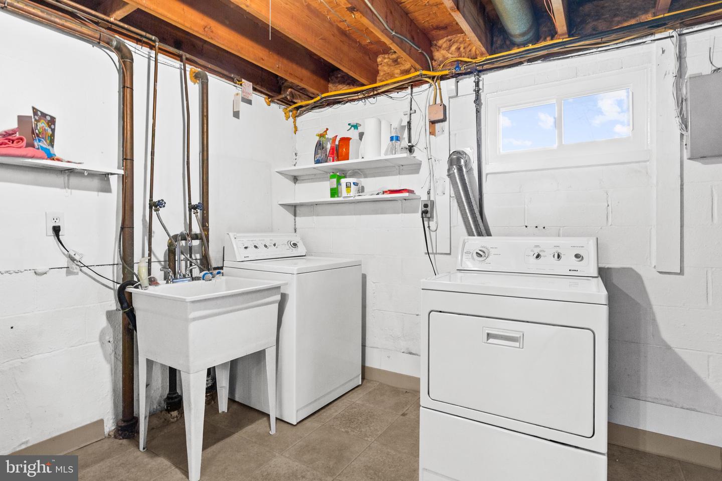 Basement laundry room with washer, dryer, deep utility sink, and exposed wooden ceiling joists.