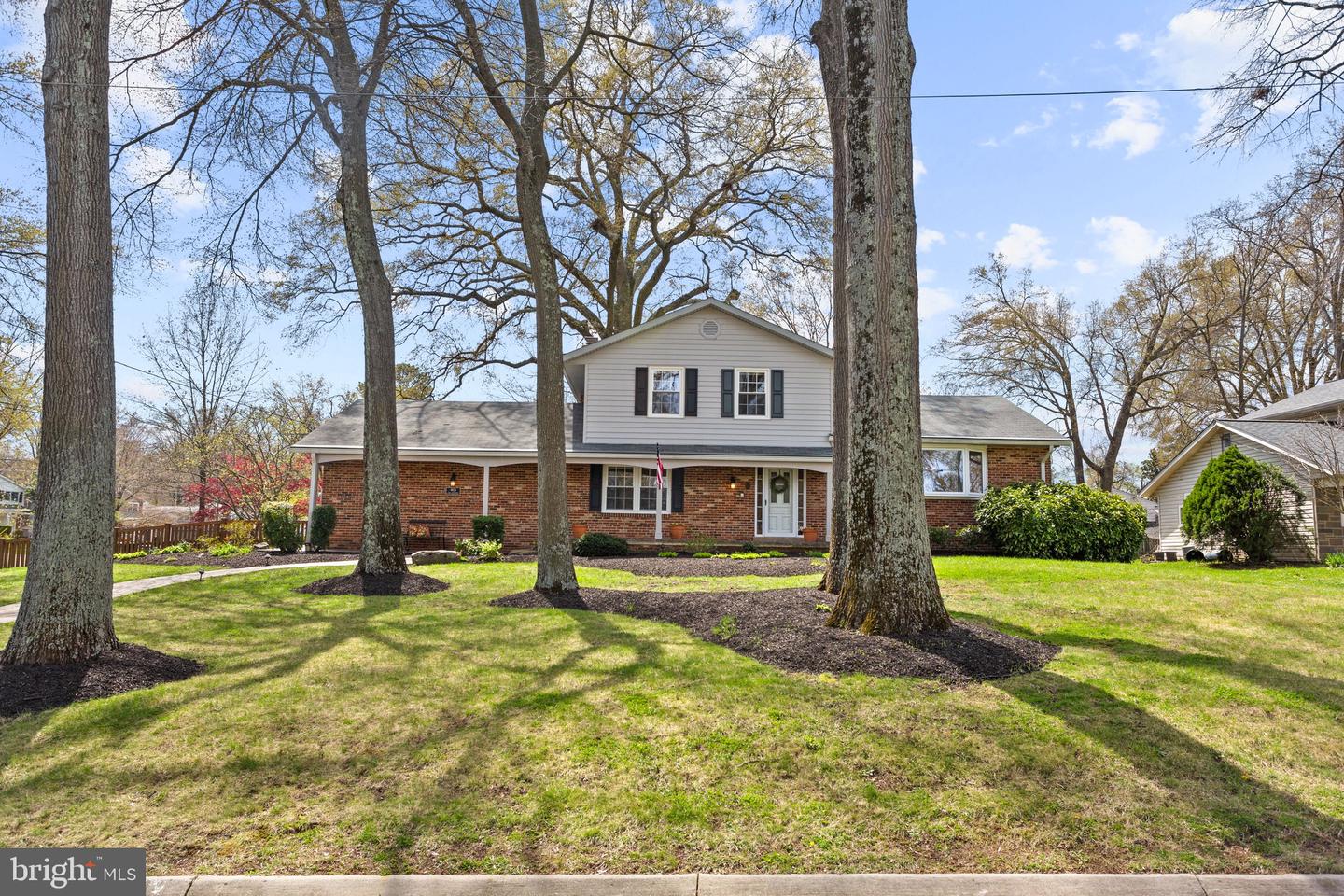 Two-story brick-and-siding home behind mature trees, with a broad front lawn.
