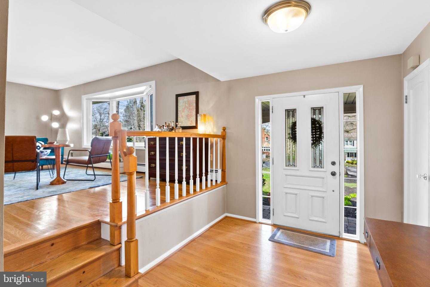 Entry foyer with hardwood floors, a wood staircase, and a white front door with glass sidelights.
