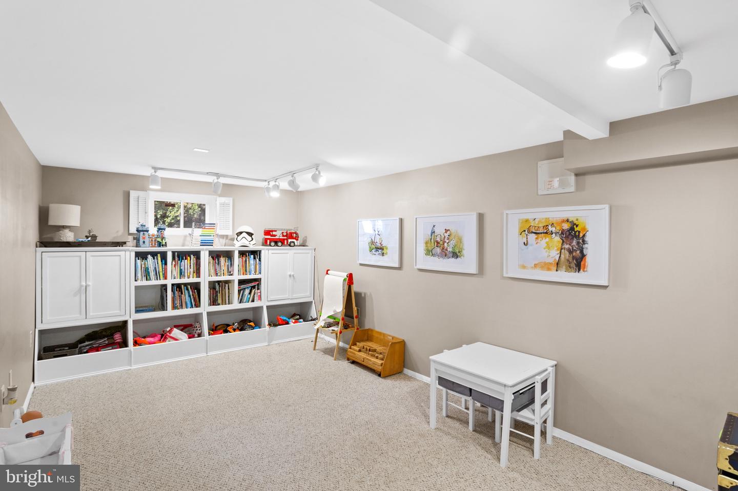 Playroom with white toy storage, bookshelves, a small table, and framed artwork.