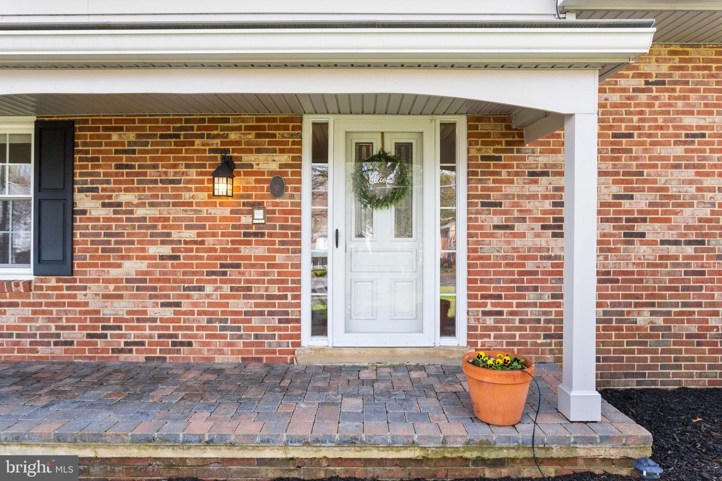 Brick home entry with a white door, welcome wreath, and paver porch.
