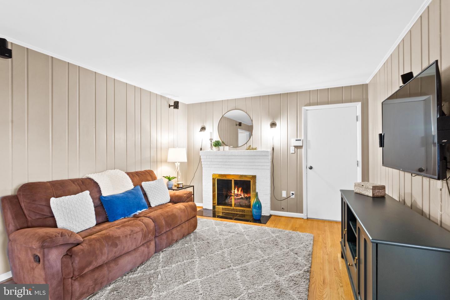 Living room with a brown leather sofa, white brick fireplace, gray rug, and wall-mounted television.