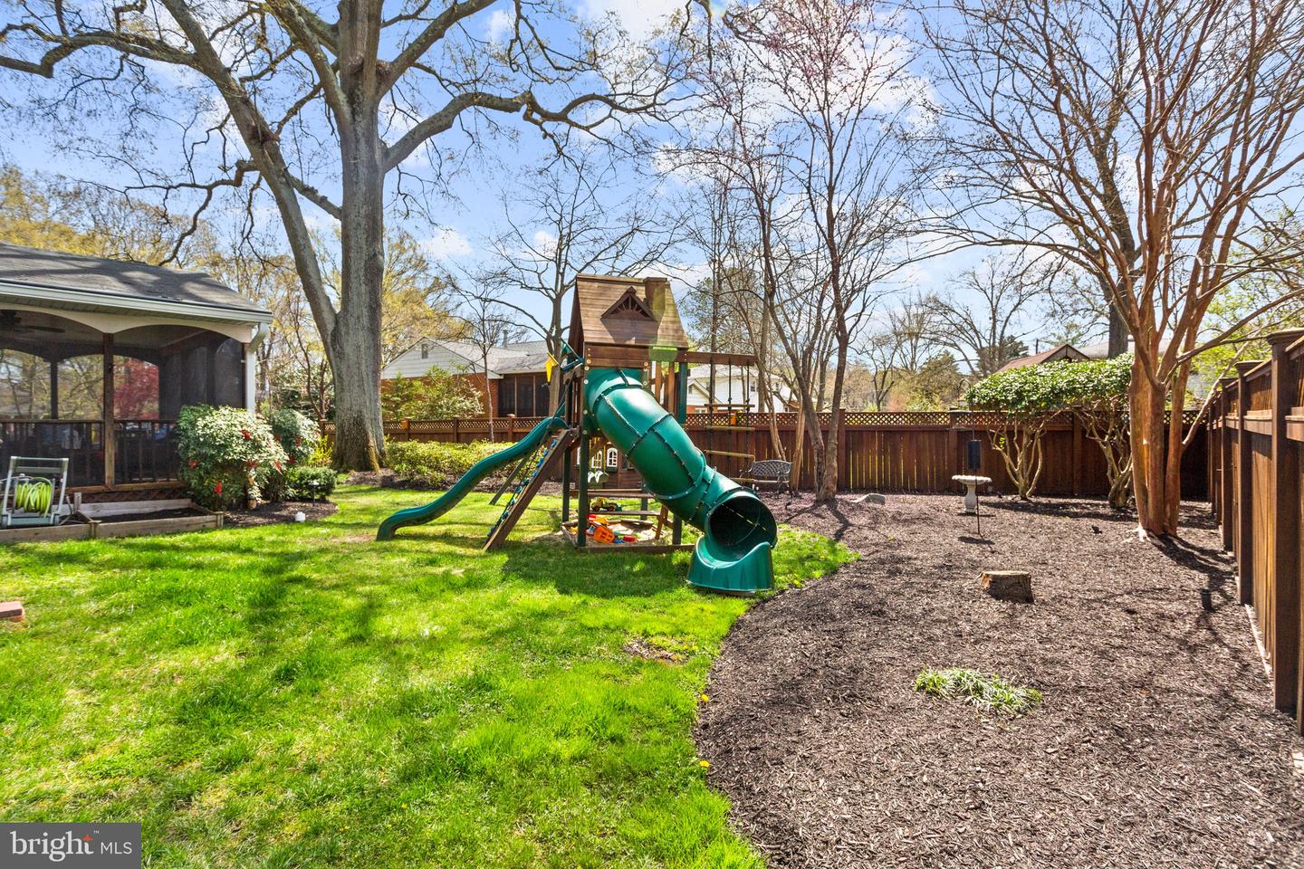 Fenced backyard with a large wooden playset, green tube slide, lawn, and screened porch.