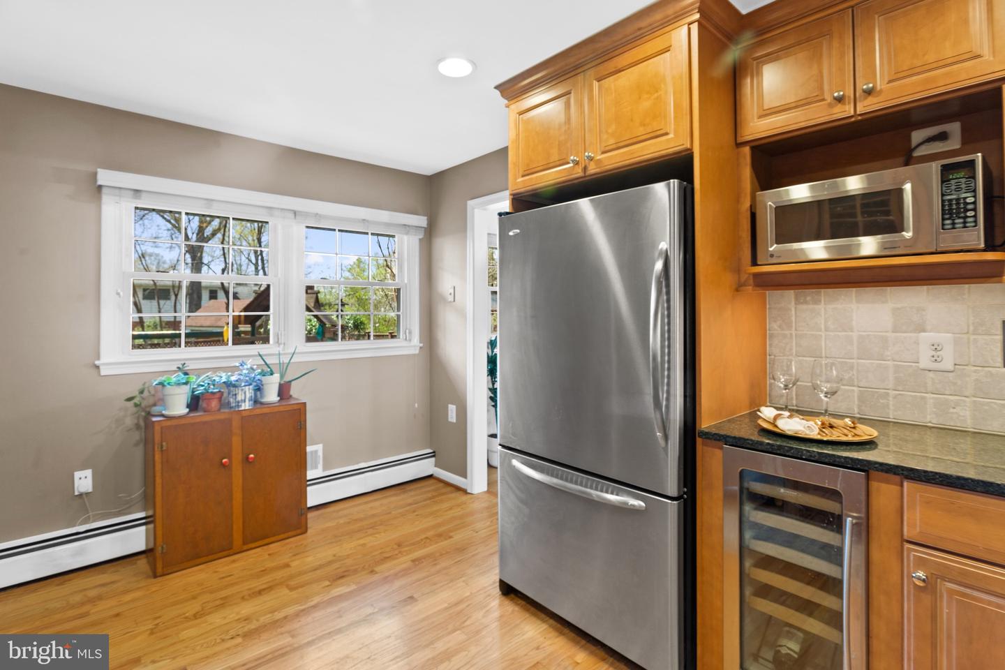 Kitchen with honey-colored cabinets, stainless steel appliances, hardwood floors, and two windows.
