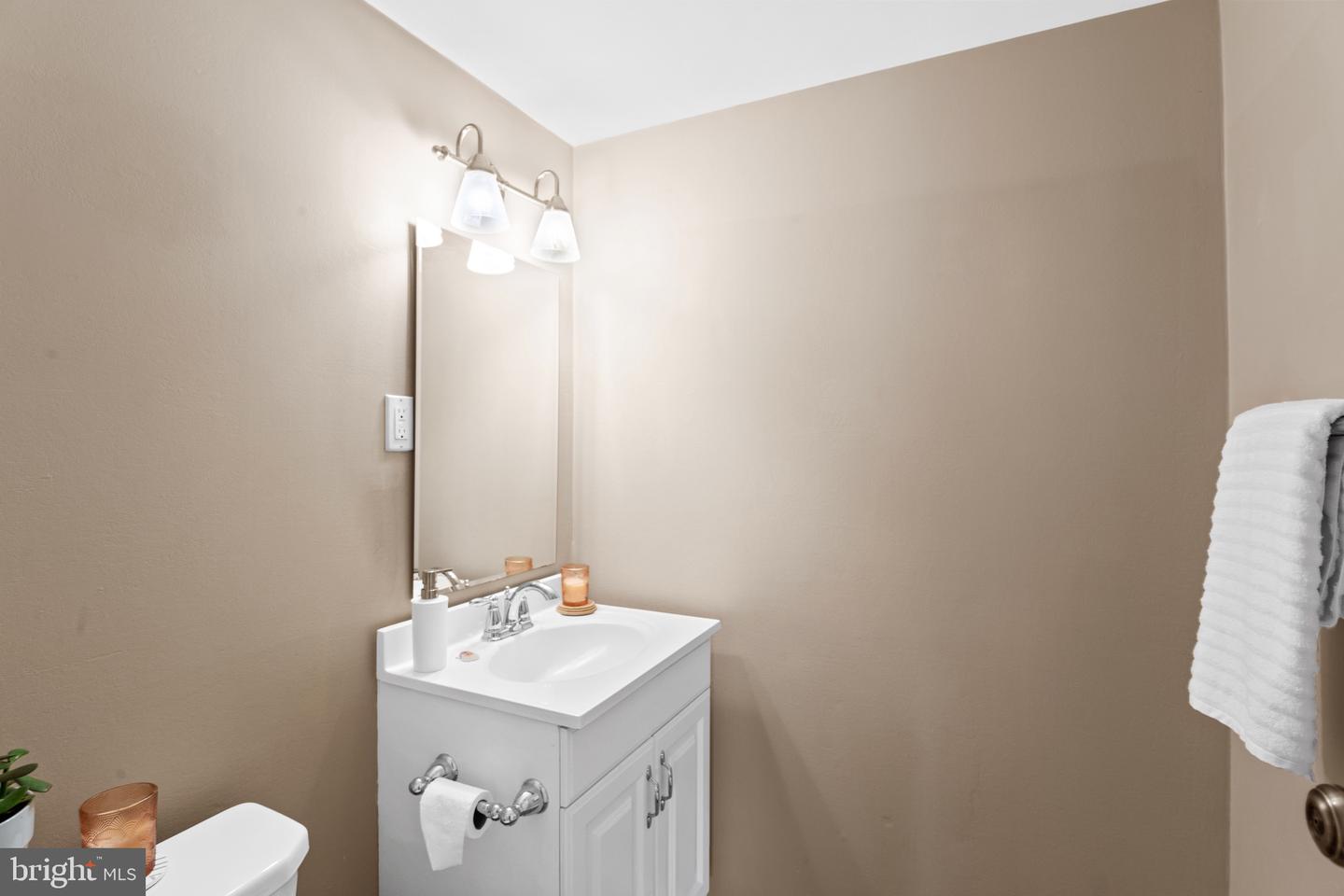 Bathroom with a white vanity, mirrored wall, two-light fixture, and beige walls.