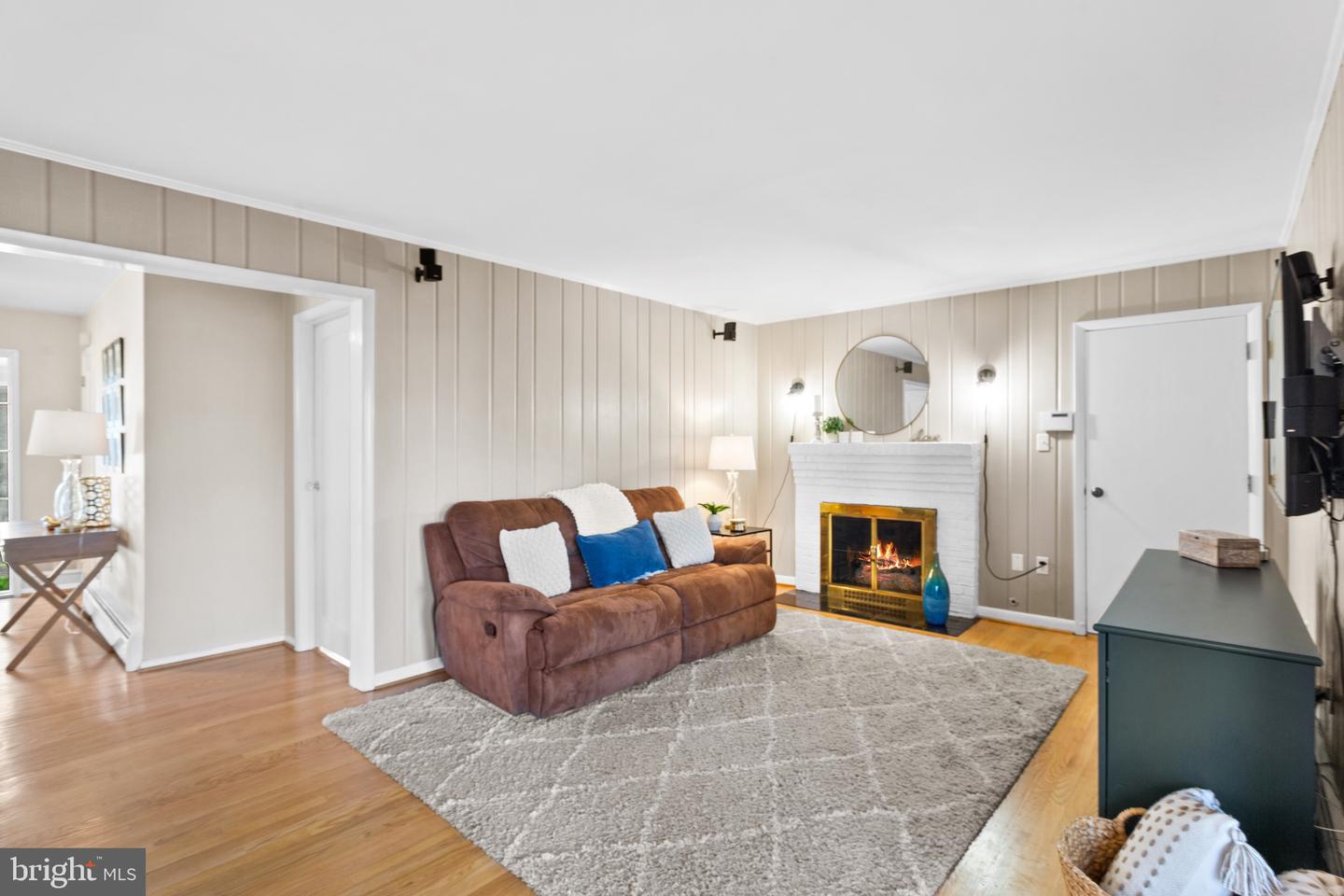 Living room with a brown sofa, gray rug, and lit fireplace beneath a round mirror.