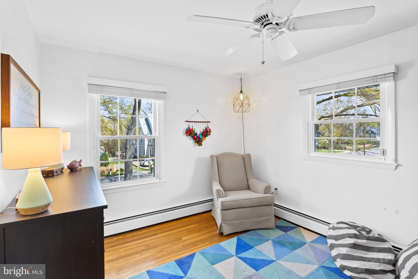 Bedroom with hardwood floors, two windows, a gray armchair, and a blue geometric rug.