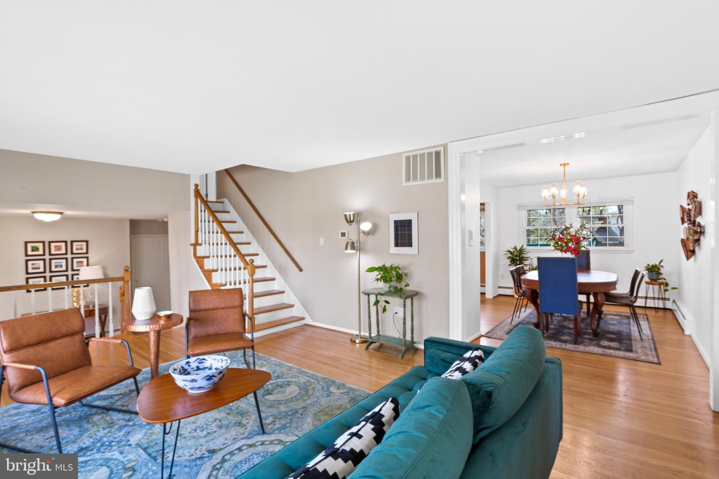 Living room with teal sofa and leather chairs, open to a dining room beside the staircase.