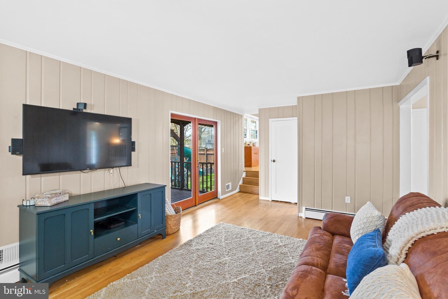 Furnished living room with a wall-mounted TV, teal media console, and glass doors to a deck.