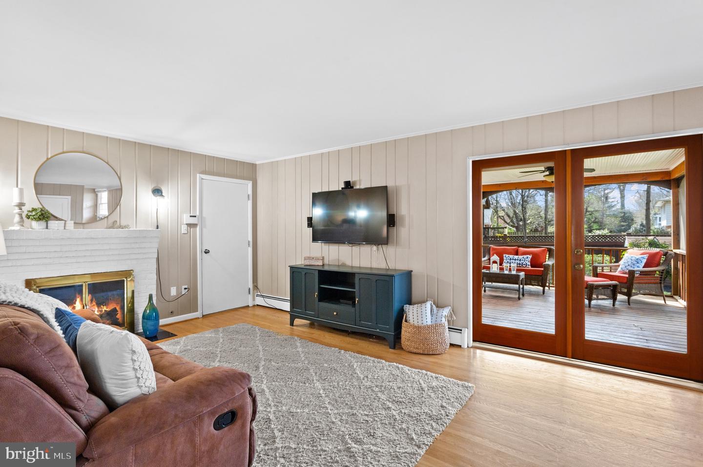 Living room with a white brick fireplace and glass doors opening to a furnished deck.