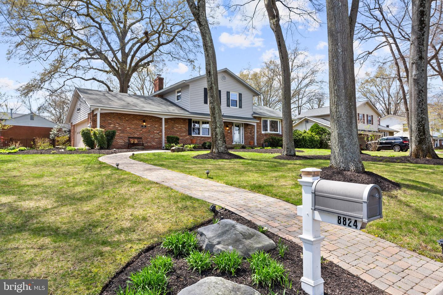 Two-story brick and gray-sided home behind mature trees, with a curved walkway and mailbox marked 8824.