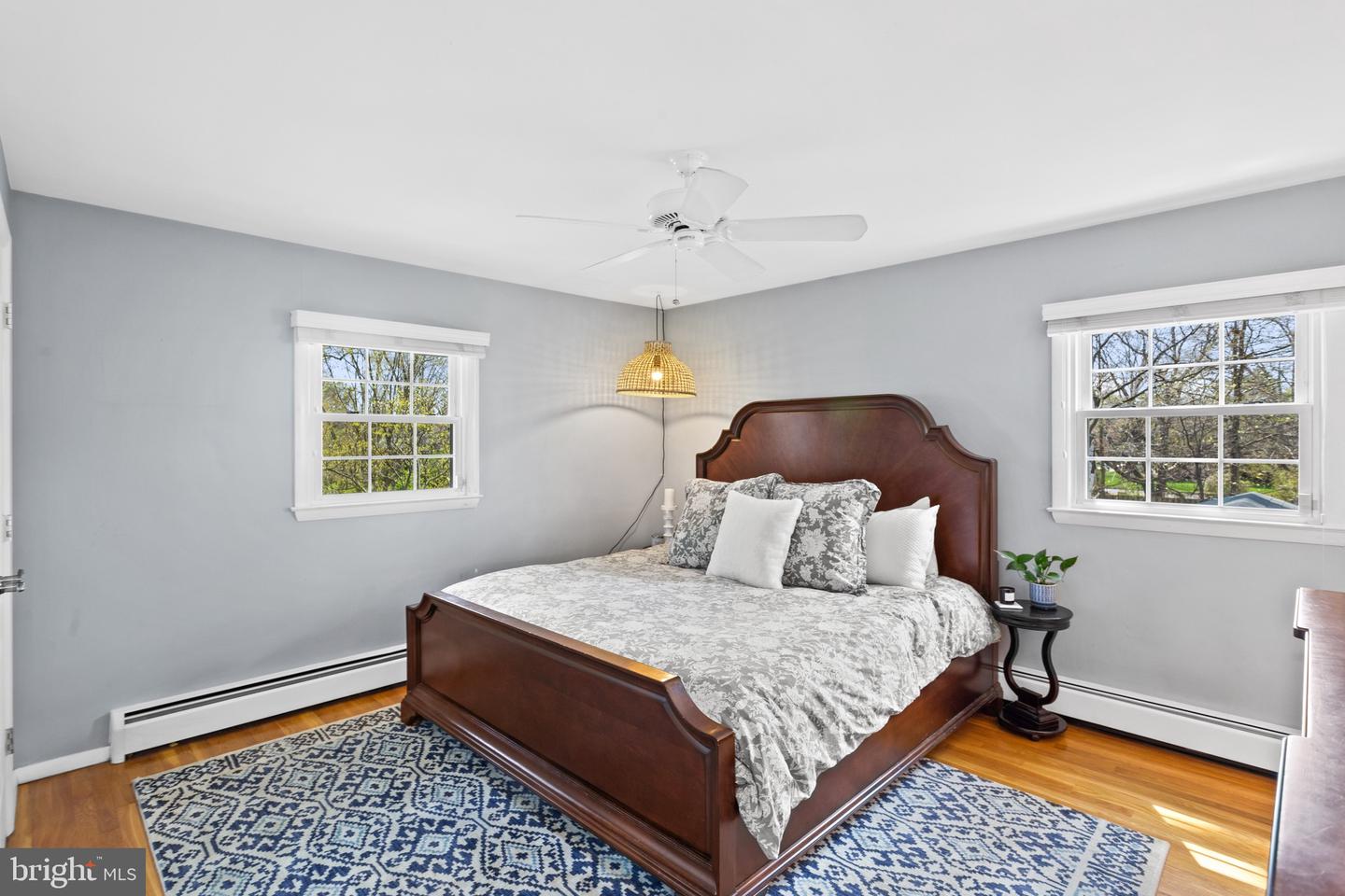 Bedroom with a dark wood bed, patterned bedding, two windows, and hardwood floors.