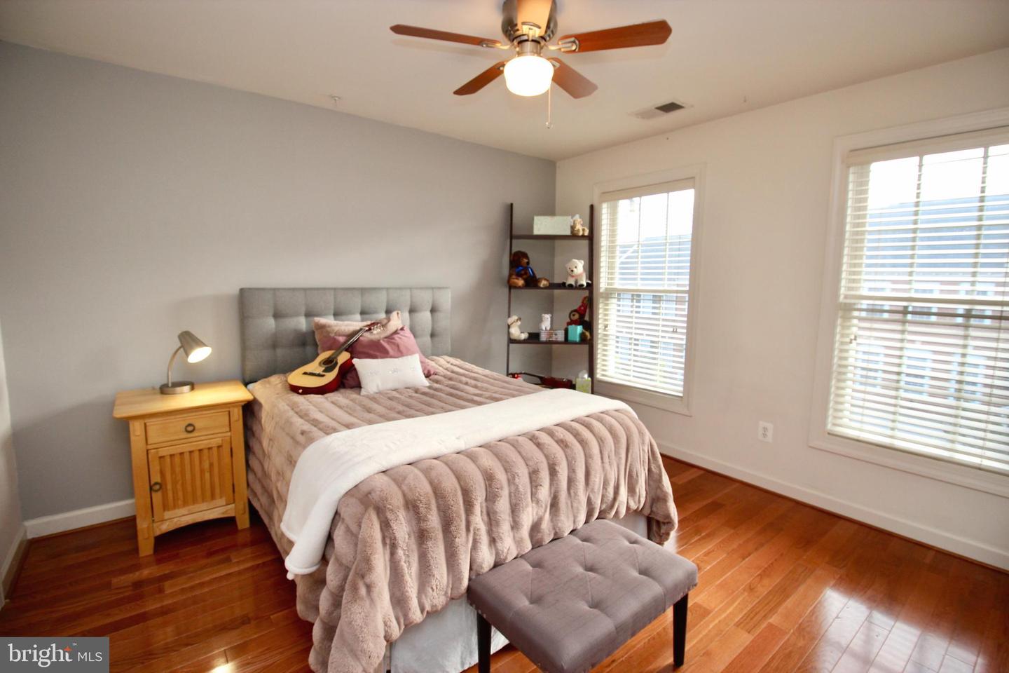Bedroom with mauve bedding, a guitar on the bed, hardwood floors, and two bright windows.