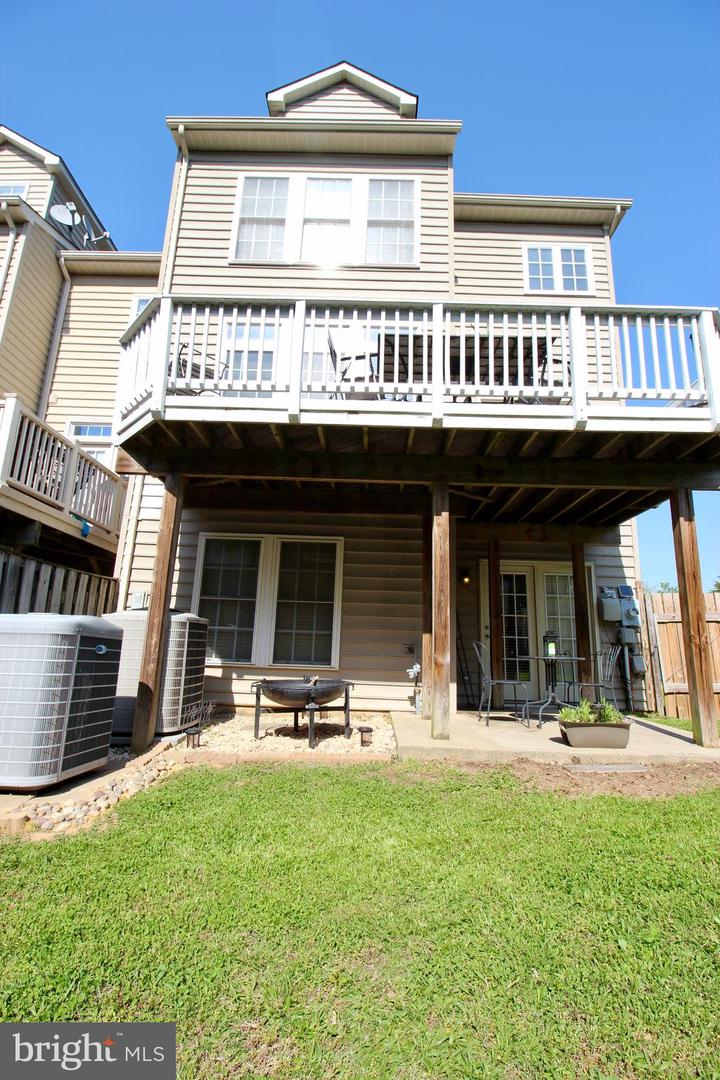 Rear of a beige house with a raised deck, covered patio, and green lawn.