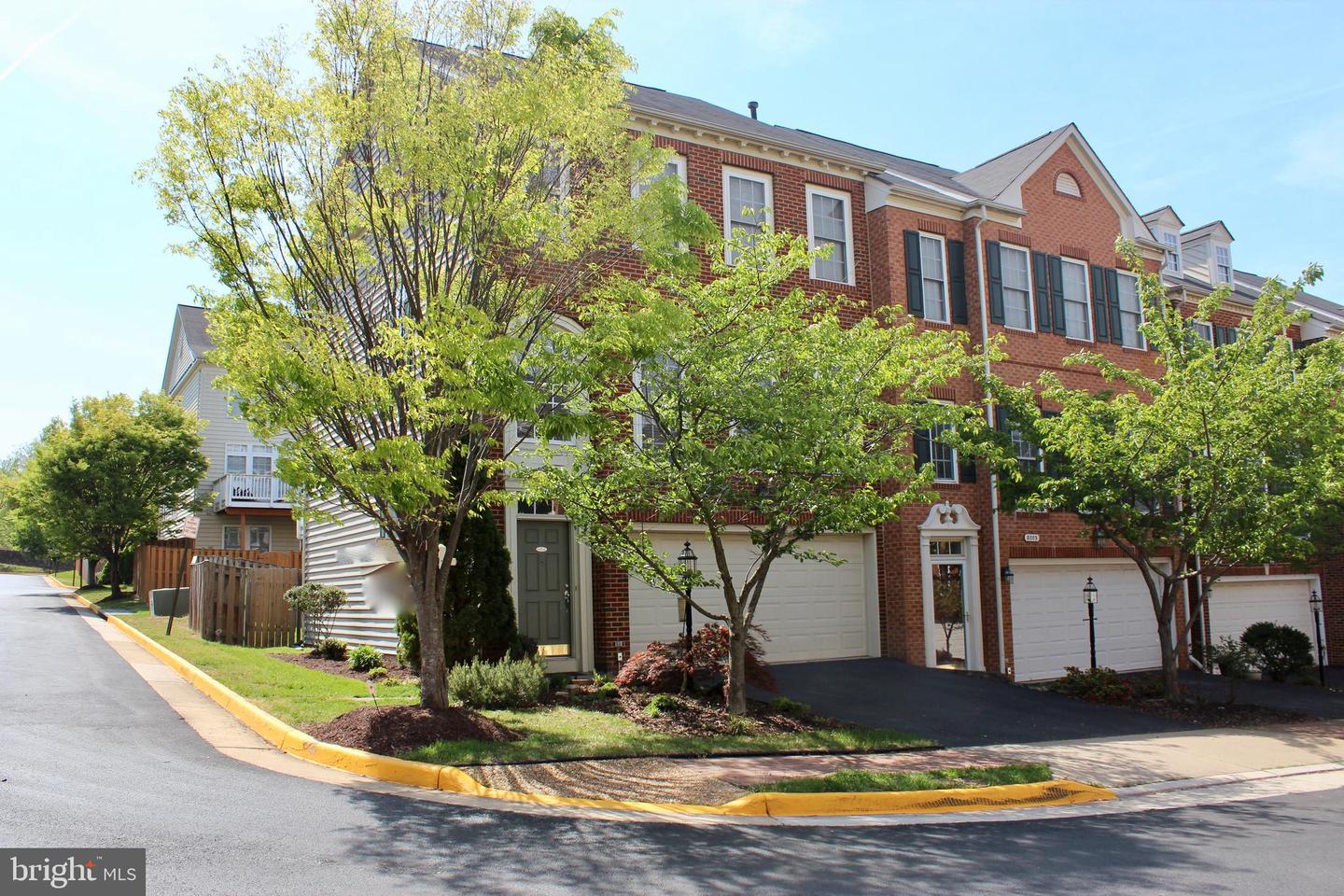 Red-brick townhome with dark shutters and an attached garage, partly screened by leafy trees.