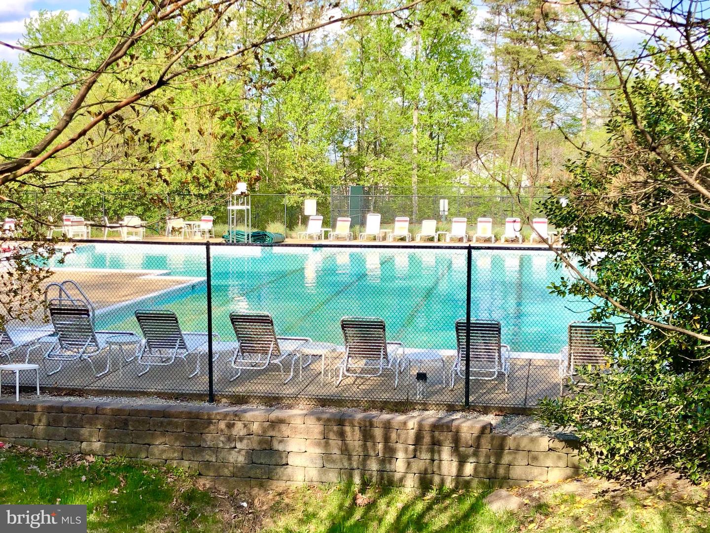 Community swimming pool with a fenced deck, lounge chairs, and trees.