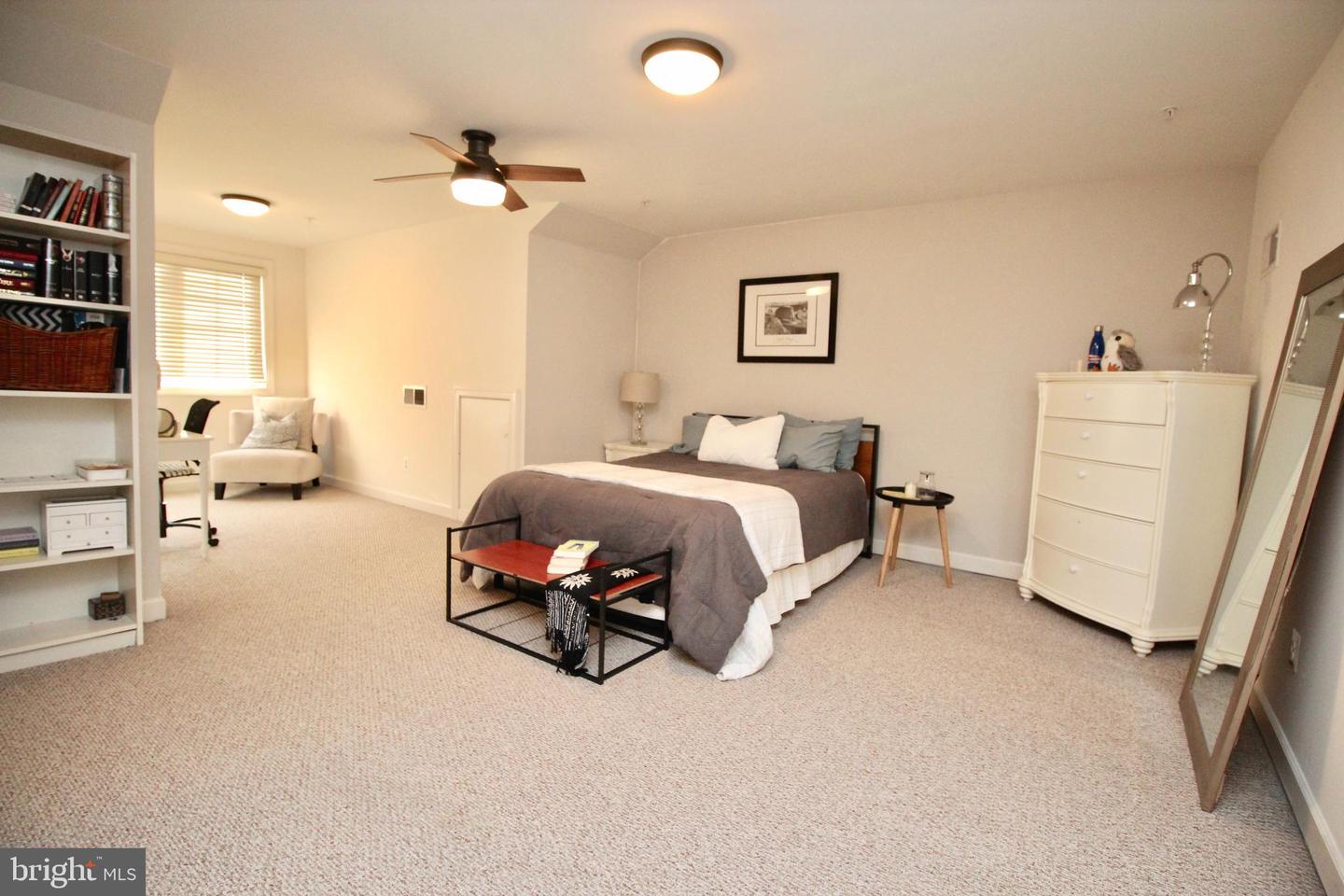 Spacious bedroom with a gray-and-white bed, built-in bookshelves, ceiling fan, and full-length mirror.