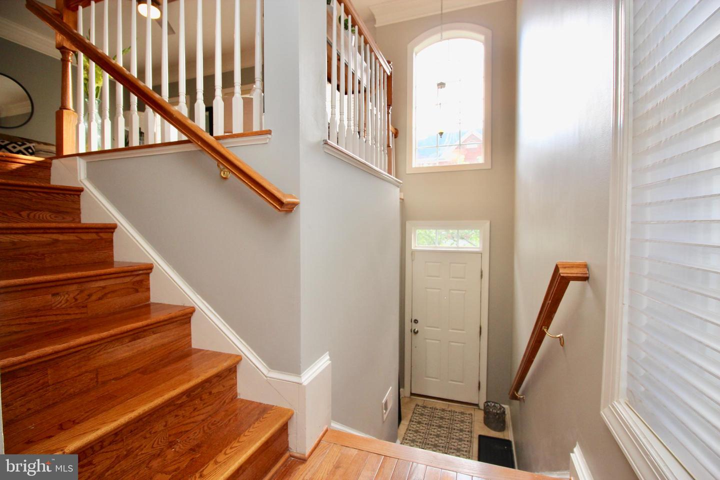 Foyer with a polished hardwood staircase, white balusters, and a tall arched window above the front door.