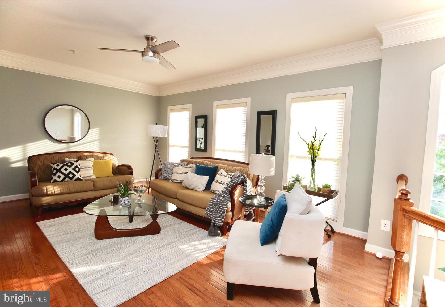 Living room with tan leather sofas, hardwood floors, and sunlight streaming through tall windows.