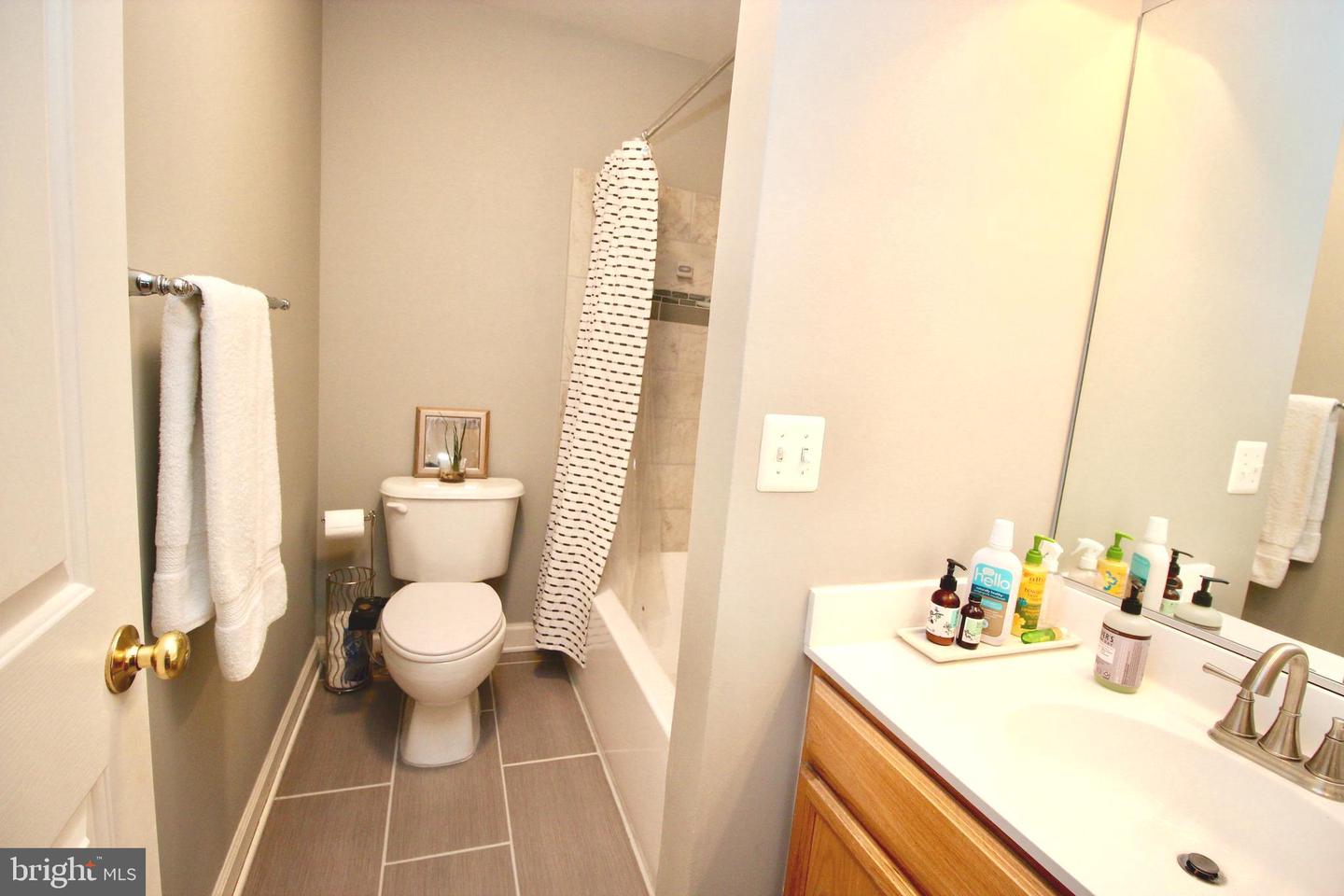 Bathroom with a white toilet, striped shower curtain, and wood vanity beneath a large mirror.