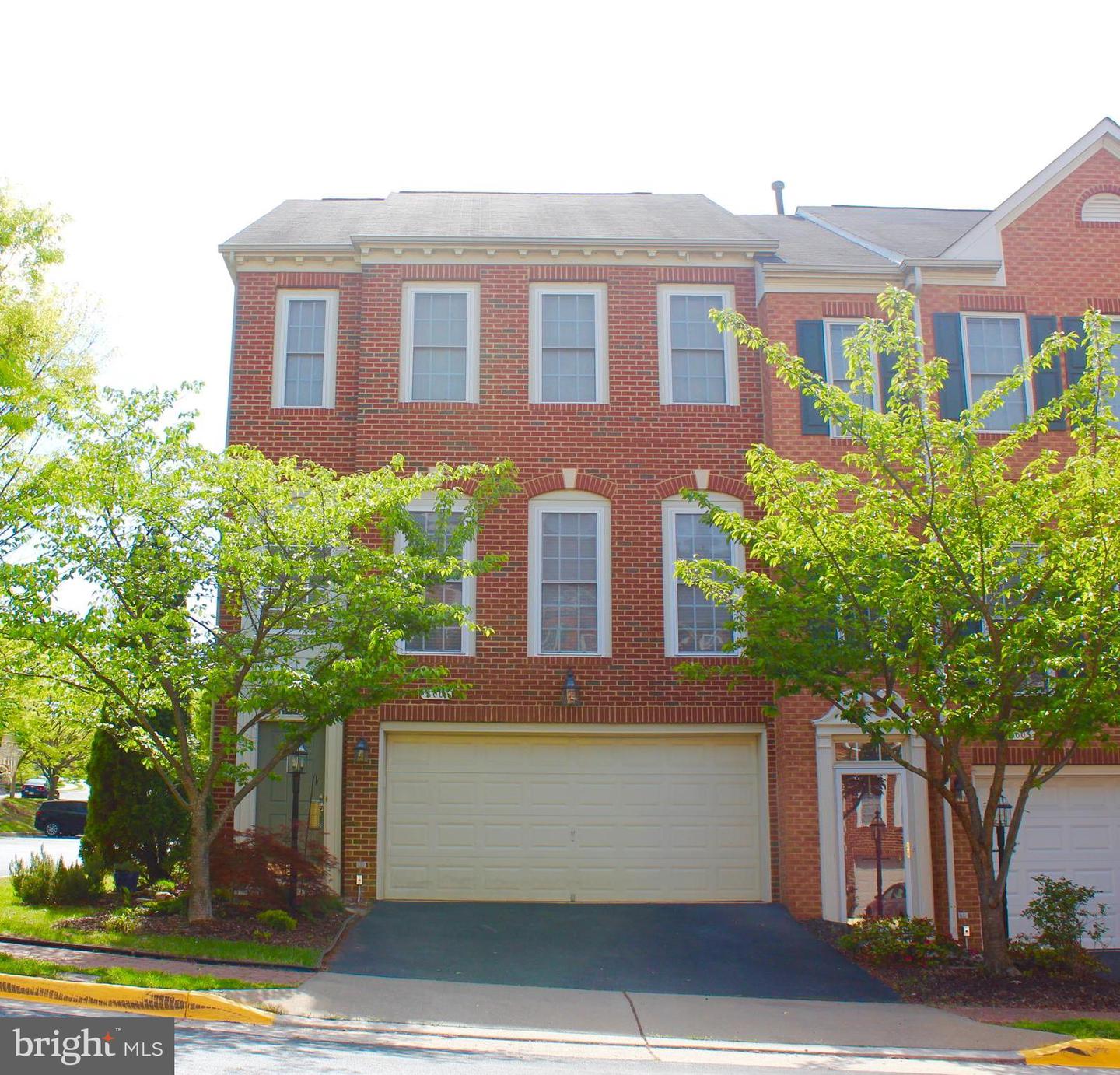 Red brick townhouse with a wide garage and leafy trees in front.