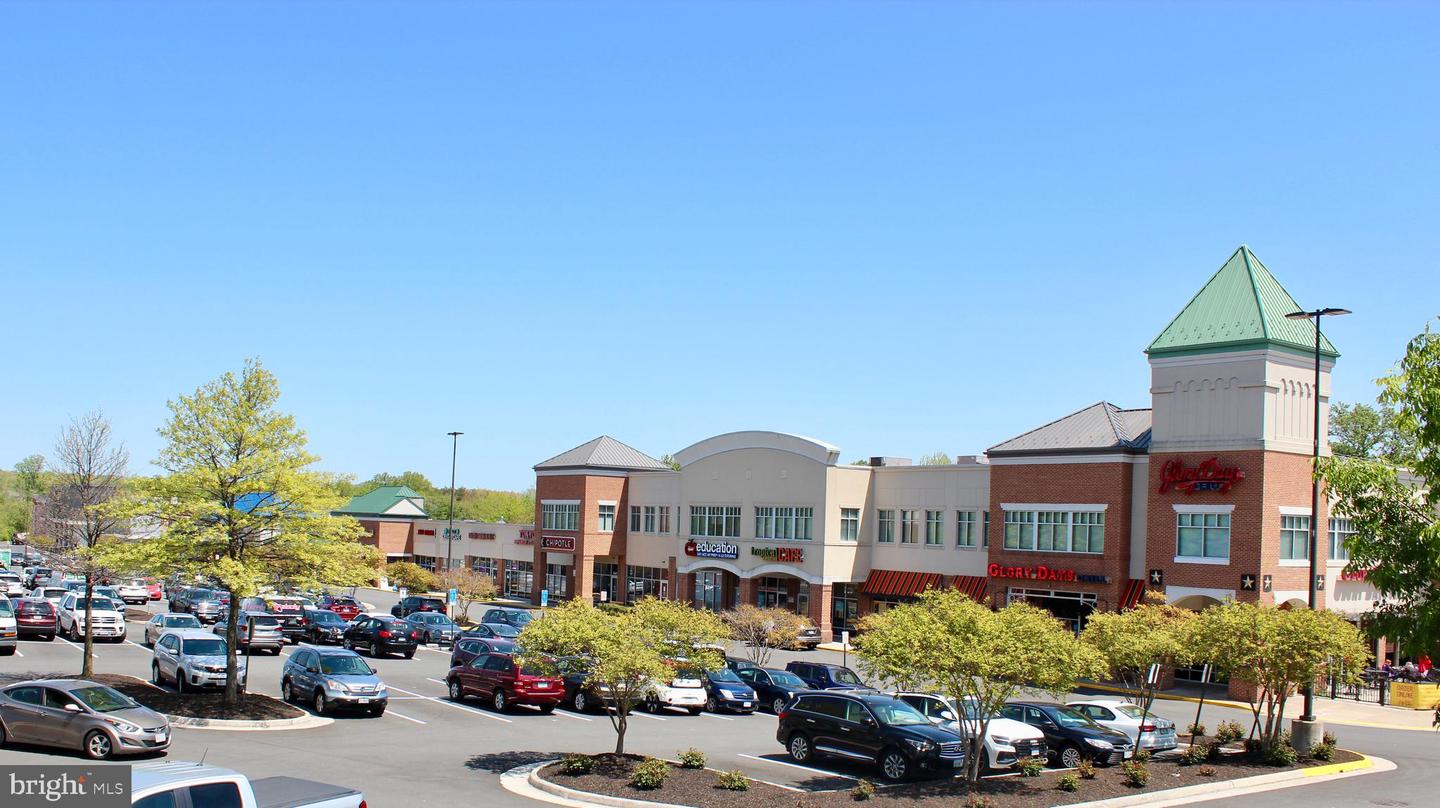 Retail shopping center with brick storefronts, a green-roofed tower, and a busy parking lot.