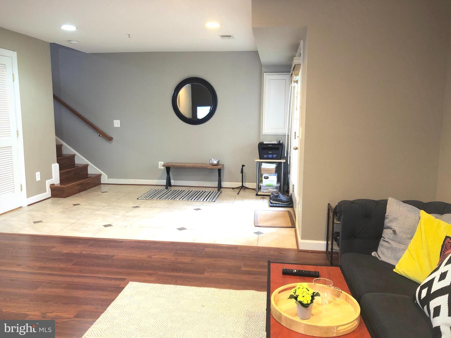 Tiled entry beside a living room, with a staircase, round wall mirror, and dark sofa.