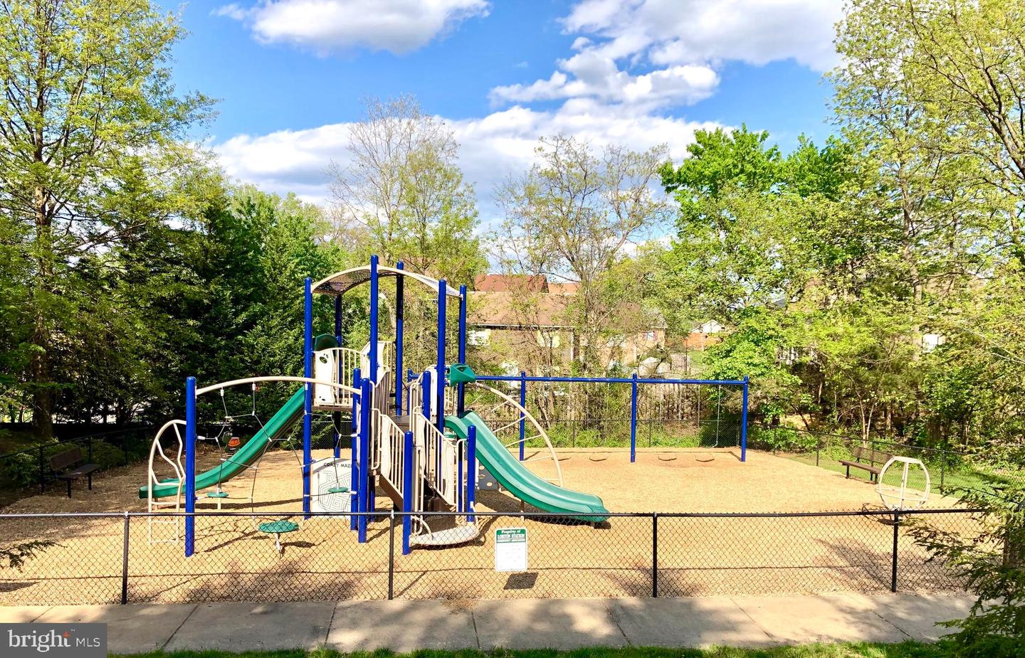 Community playground with blue and green slides and swings inside a fenced play area.