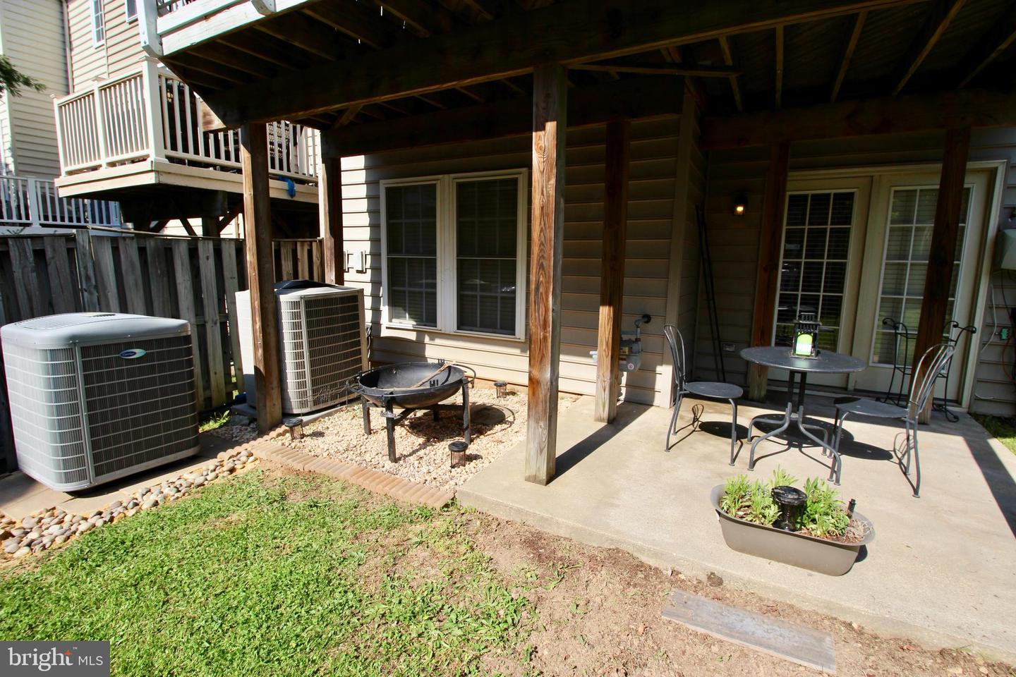 Covered backyard patio with outdoor table, chairs, and a fire pit beneath a raised deck.