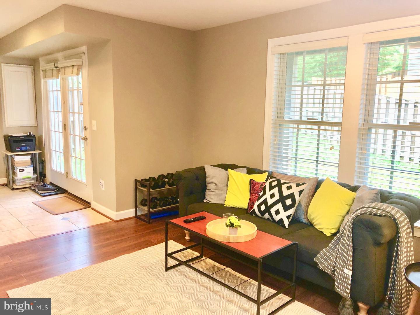 Living room with a tufted sectional, colorful pillows, a coffee table, and large windows with blinds.