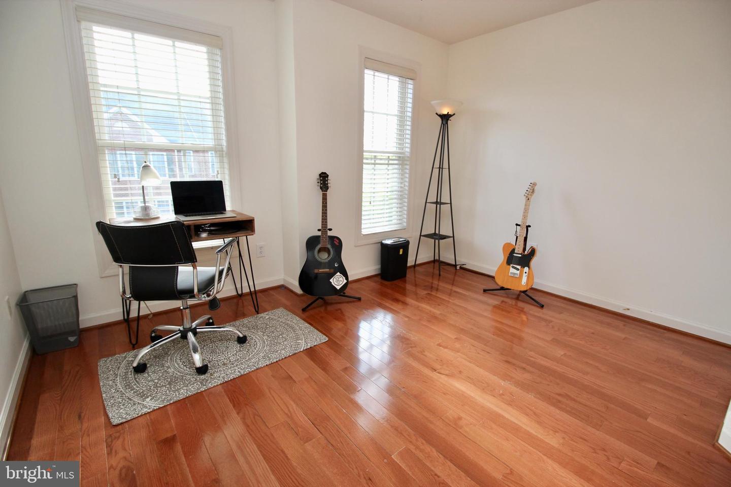 Home office and music room with hardwood floors, two windows, a desk, and guitars.