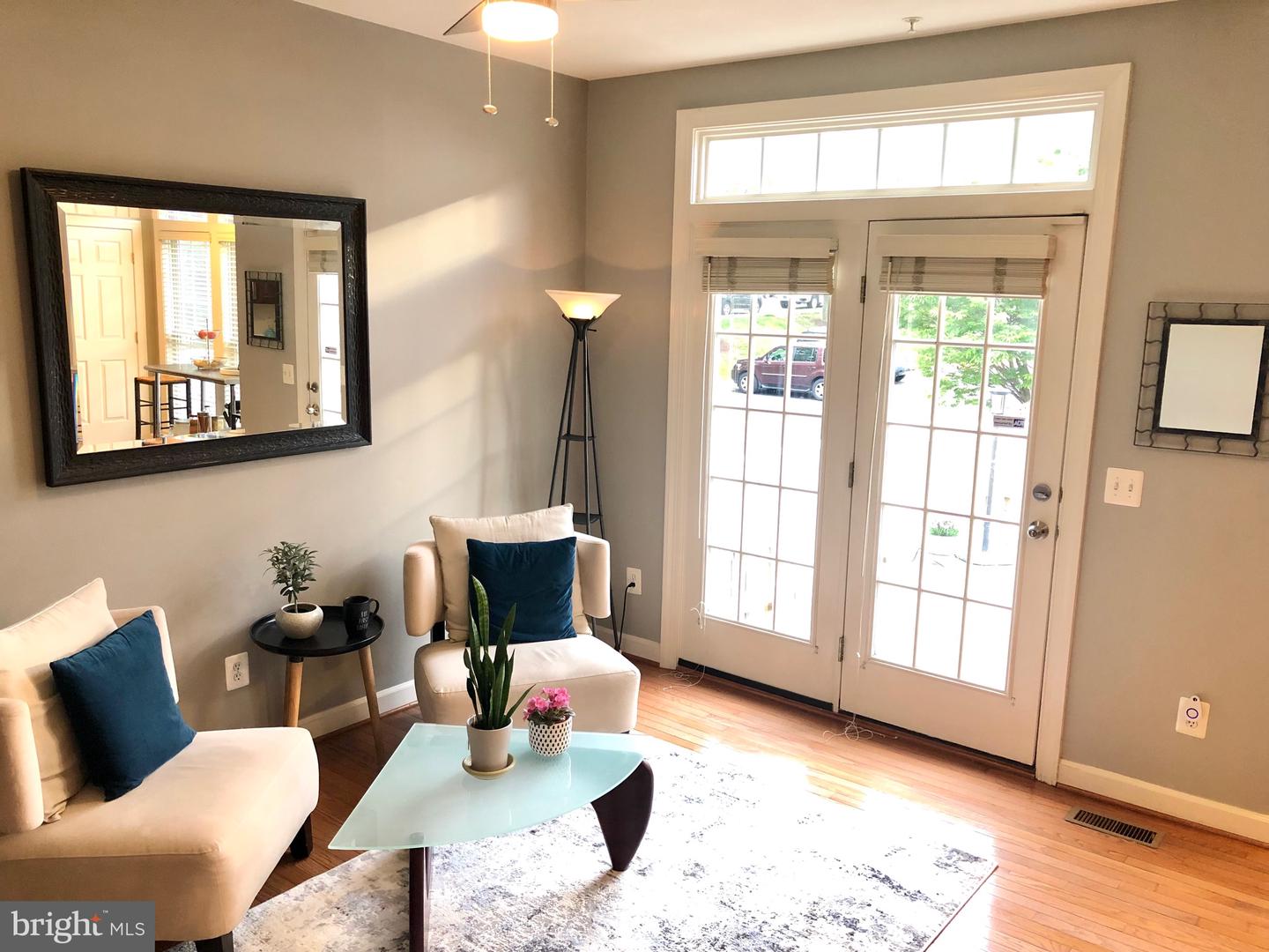 Staged living room with cream armchairs, blue pillows, hardwood floors, and bright French doors.