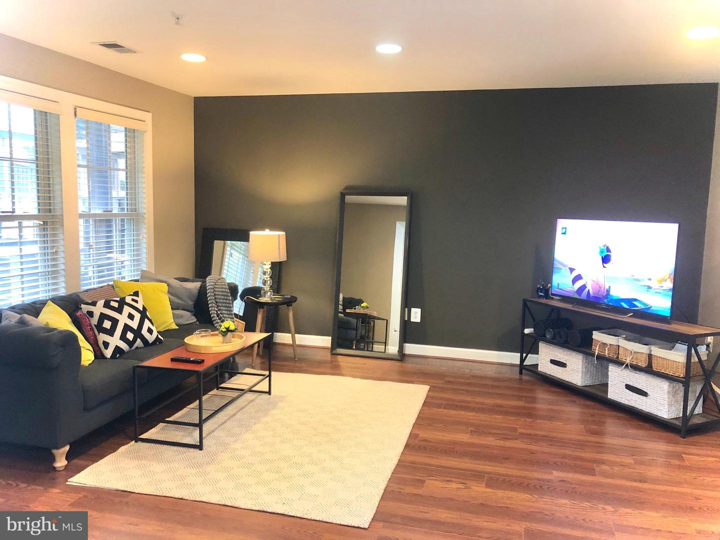 Living room with a charcoal sectional, cream rug, dark accent wall, and television.