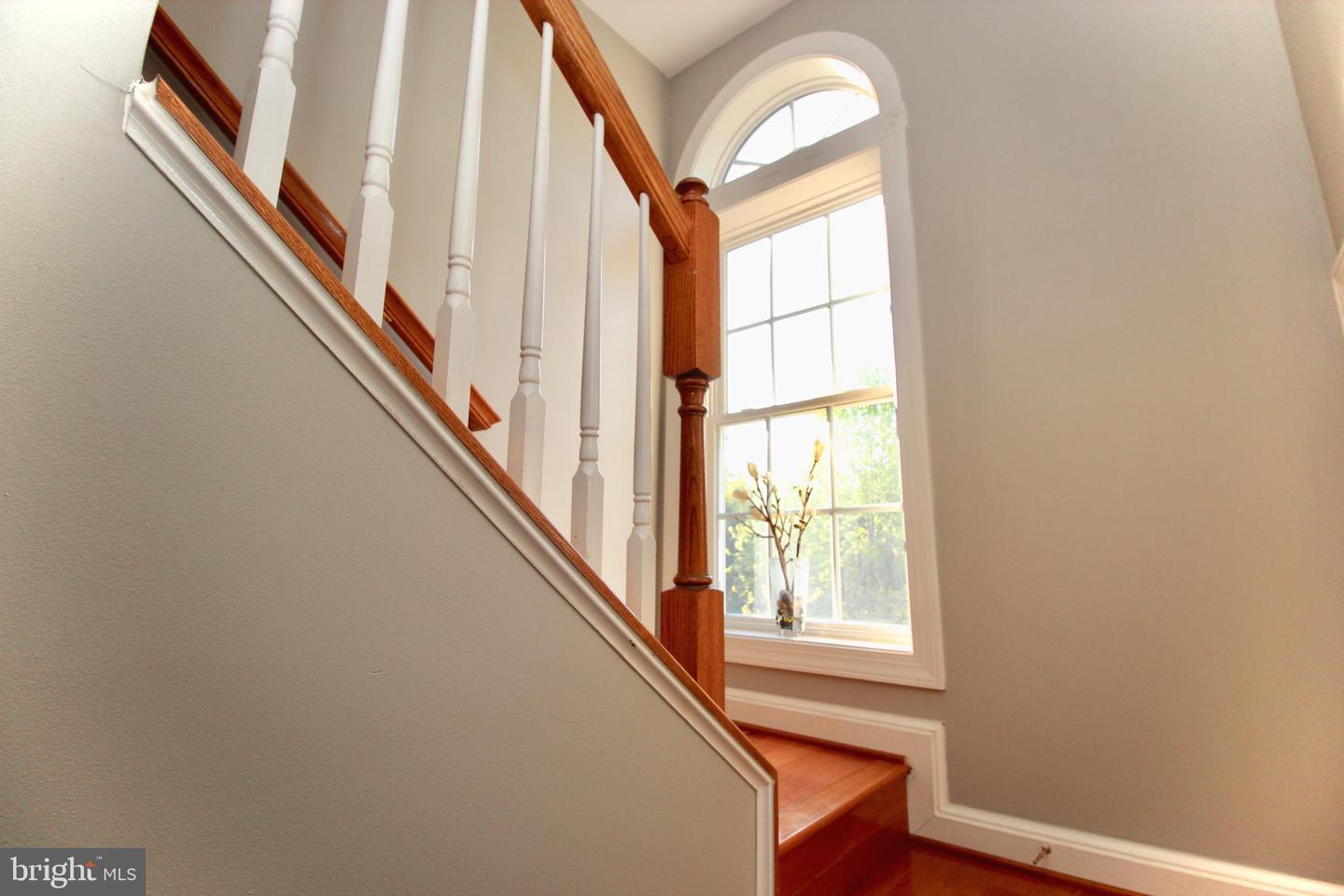 Staircase with wood treads and railing beside a tall arched window.